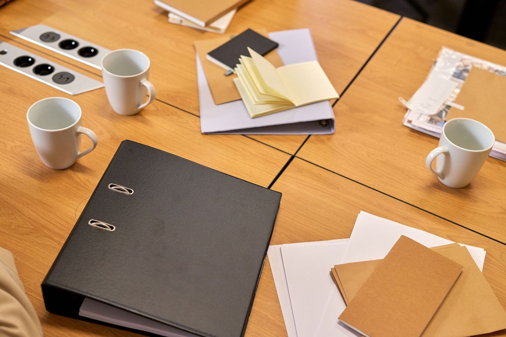 Open notebooks, binders, papers, and mugs arranged on a worktable